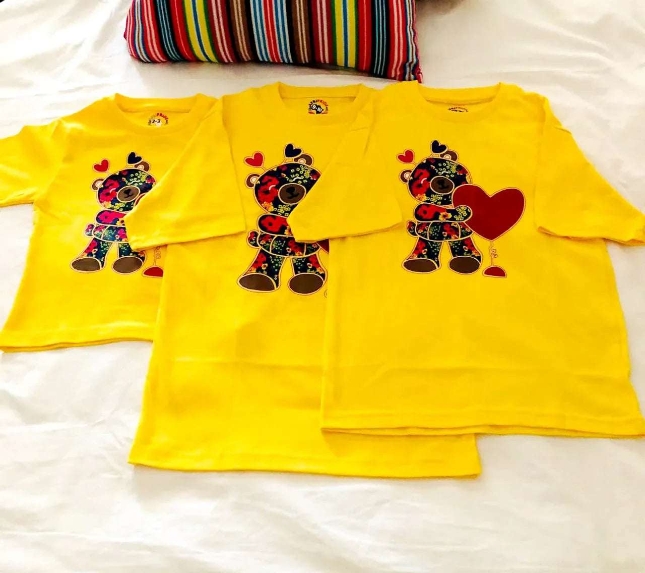 Bright yellow unisex kids T-shirts featuring colorful African fabric-inspired teddy bear and heart designs, made from 100% cotton for comfort.