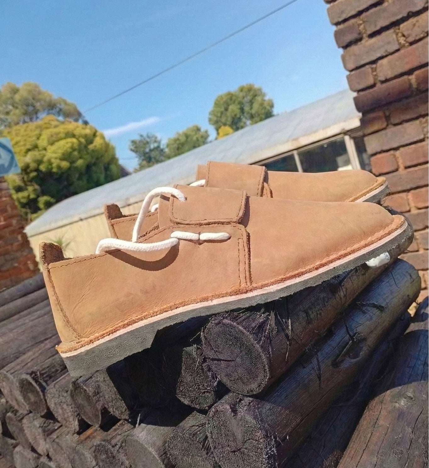 Brown leather shoe with white laces on a stack of firewood outdoors.