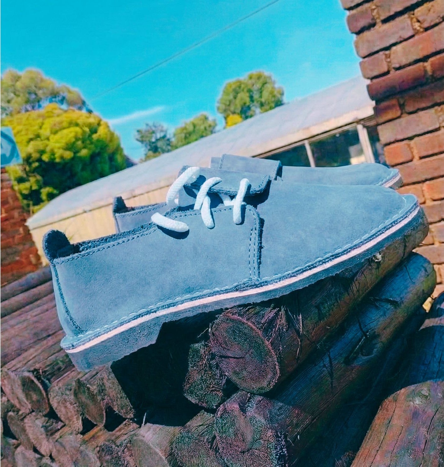 Blue genuine leather shoes with white laces on a stack of firewood against a brick wall and blue sky.