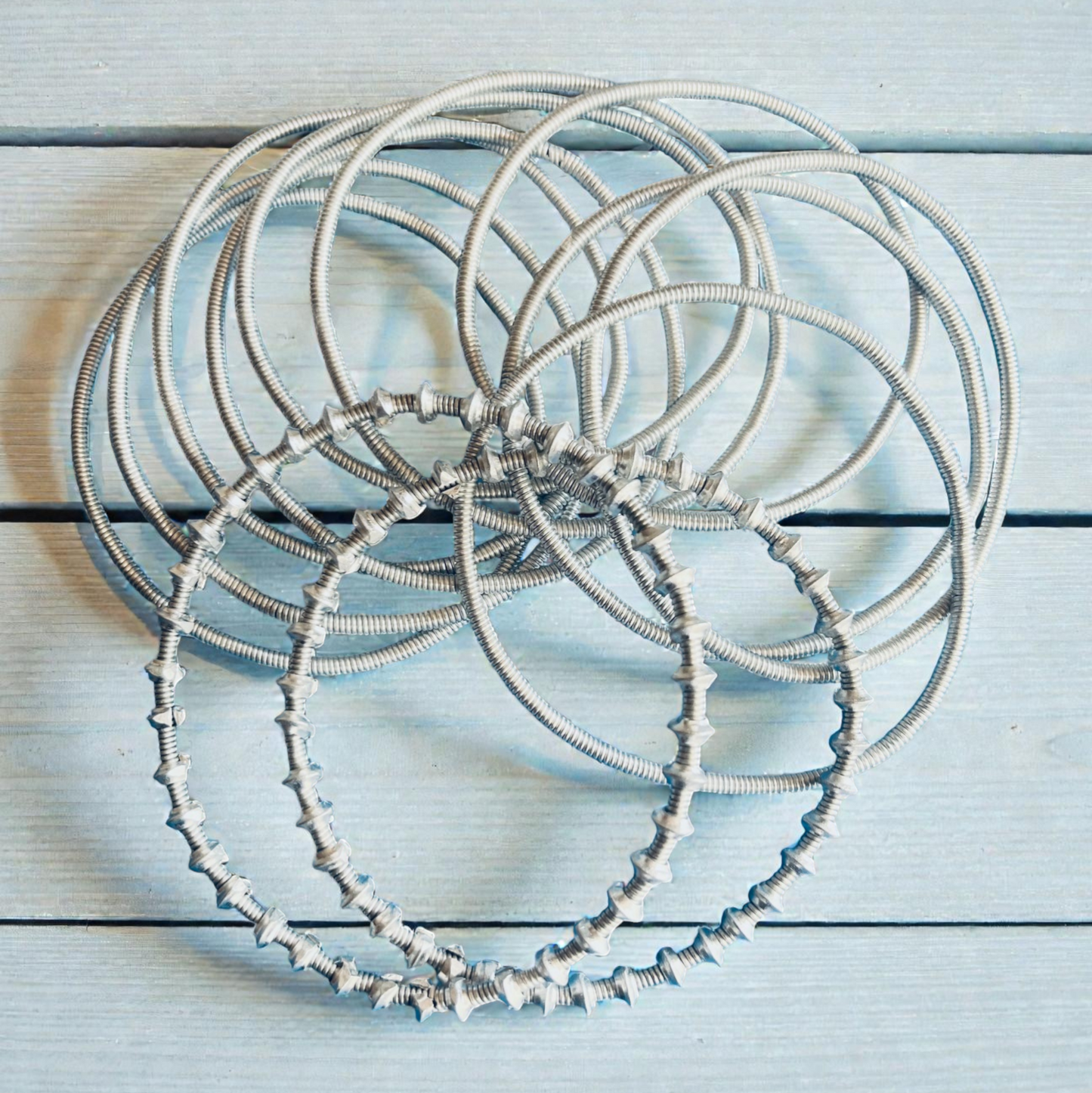 Set of silver aluminium Venda Bangles on a light blue wooden surface