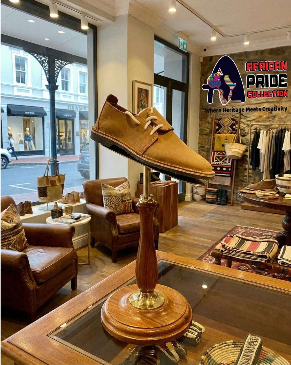 Brown leather vellie shoe on a wooden stand in a store with 'African Pride Collection' branding.
